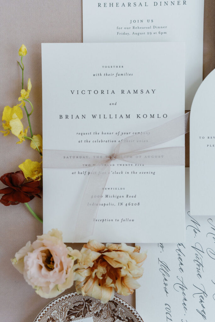 Wedding flatlay featuring luxury invitations, antique toile ring dishes, and calligraphed envelopes.
